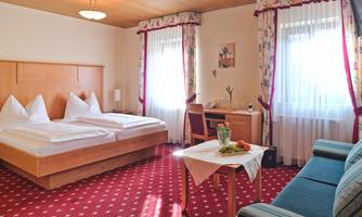A cozy room with two single beds and a blue sofa. A table with fruit and a small vase is also available.