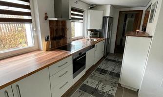 A modern kitchen with a wooden countertop and white cabinets. The floor is covered with a stylish printed carpet.