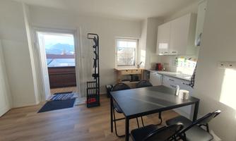 A bright and modern kitchen with a dining table and chairs. Large windows offer a view of the mountains.