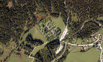 An aerial shot of a forest area with a planned construction project in the middle. Surrounded by trees and a small settlement nearby.