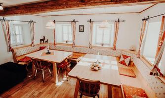 A cozy dining area with wooden panels and padded benches. Bright walls and windows make the room appear inviting.