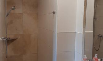 A modern bathroom with a shower and a sink. The walls are tiled in light colors, and a red towel is placed on the sink.