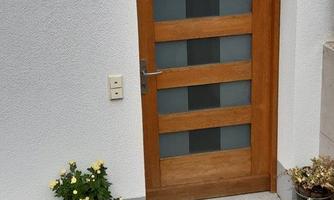 A wooden front door with glass elements. Next to the door, there are flowers in pots.