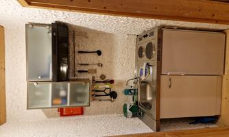 A small kitchenette with sink, cooking plates, and kitchen utensils. The walls are light, and the furniture is made of wood.