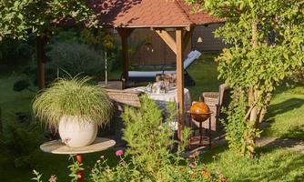 A cozy garden with a pavilion and colorful flowers. In the background, there is a table inviting you to relax.