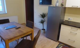 A cozy kitchen with a wooden table and chairs. In the background, there is a refrigerator and a potted plant.
