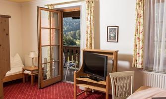 A cozy room with an open balcony and a view of nature. The decor is simple and inviting, featuring a television and a dining area.