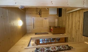 An inviting entrance area with wooden walls and a light wooden floor. In front of the door, there is a coat rack and a piece of furniture for storage.
