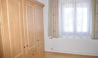 A bright room with a wooden wardrobe and a window. The curtains are light and let in light.