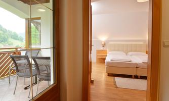 A cozy bedroom with a large bed and a balcony. The room has a bright, modern design and a view of the green landscape.