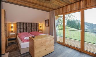 A cozy bedroom with a double bed and wooden elements. Large windows offer a view of the green landscape.