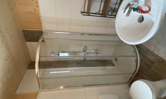 A modern bathroom with a glass shower cabin. The furnishings include a sink and a toilet, as well as a small shelving unit.