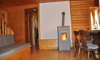 A cozy room with wooden walls and a wood stove. A comfortable seating area and a dining table complete the atmosphere.