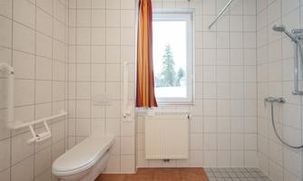 A bright bathroom with white tiles and a window. There is a toilet, a shower rod, and a towel holder.