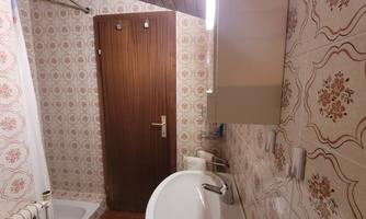 A small bathroom with a bathtub, a sink, and a wooden portal. The walls are decorated with floral tiles.