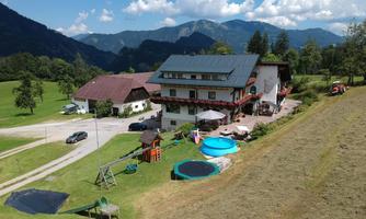 A modern house amidst a picturesque landscape with mountains in the background. In the foreground, there are play and water areas for children.