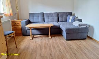 A living room with a gray couch and a small wooden table. The floor is made of wood and there is a chair as well as a cabinet in the room.