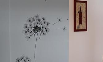 A wall with stylized plant drawings in black and white. In the background, a painted image in red and beige is visible.
