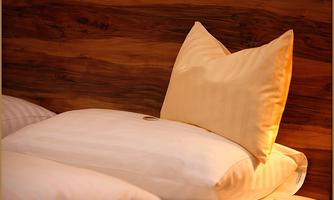 Cushions on a bed with a warm wood background. A beige cushion stands behind a white cushion.