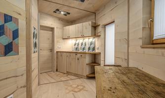 A modern kitchen with wooden panels and a large table. The walls are bright and there are colored wall coverings.