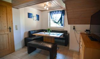 A cozy dining area with a bright atmosphere. There is a table, black seating, and a small decoration with fresh flowers.