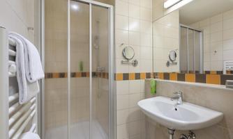 A modern bathroom with a shower, a sink, and a large mirror. The walls are lightly tiled, and there are towels ready.