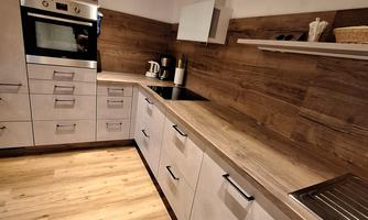 A modern kitchen with wooden cladding and light cabinets. The design is functional and inviting.