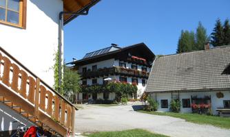 A picturesque building in a rural style with balconies and red flowers. In the foreground, there are toys on the ground and a paved path leading to the house.