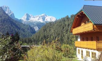 A picturesque mountain valley with snow-capped peaks in the background. In the foreground stands a cozy wooden house, surrounded by trees and plants.