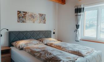 A cozy bedroom with a double bed that is equipped with blankets. The room has a window with a view and light-colored walls.