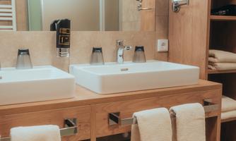 A modern bathroom with two ceramic sinks. The wooden surface and the towels create a friendly atmosphere.