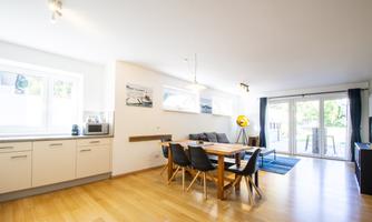 A bright and modern dining room with a large table and black chairs. The windows offer a view of the garden and let in plenty of light.