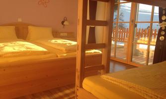 A cozy bedroom with two beds and a loft bed. Large windows let in plenty of light and offer a view of a balcony.