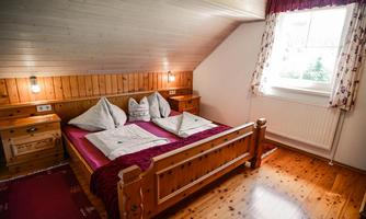 A cozy bedroom with a wooden double bed and a bright wooden ceiling. The room has a window with a view and is friendly and well-lit.