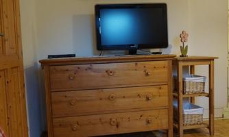 A cozy living room with a wooden table and a television. On the wall hangs a picture of a landscape.