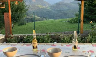 An idyllic view of green hills and mountains. On a table, there are two drinks and empty bowls, ready for an outdoor meal.