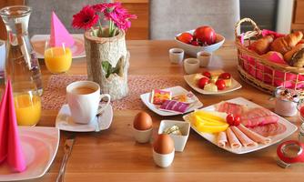 A colorful breakfast table set with fresh fruit, croissants, and various cold cuts. Alongside a glass of juice and coffee, there are decorative flowers.