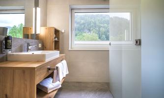 A modern bathroom with wooden shelves and a large window. The room is bright and friendly, with a clear view of nature.
