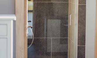 A modern shower with gray tiles and a glass door. The area is clean and well-lit.