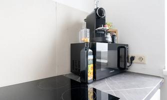 A modern kitchen with a microwave and a coffee maker. On the countertop is a bottle of olive oil.