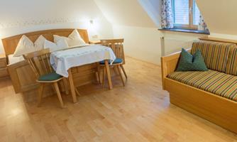 A harmoniously furnished room with a double bed, a dining table, and a cozy seating area. Bright wooden floors and soft colors create an inviting atmosphere.