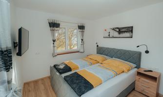 A modern bedroom with a double bed and a bedside table. Large windows let in plenty of light and the walls are brightly painted.