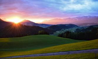 A picturesque sunrise over gentle hills and mountains. The sky is illuminated in warm colors and the landscape appears peaceful.