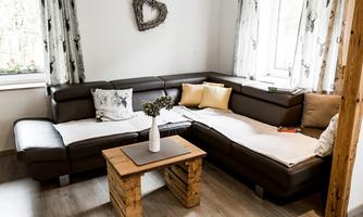 A cozy living area in brown with cushions and a small wooden tabletop. Large windows provide plenty of daylight and an inviting atmosphere.