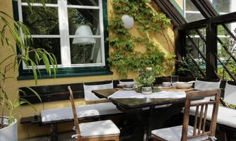 A cozy dining area with a table and chairs, surrounded by plants. The light falls through the windows, creating an inviting atmosphere.