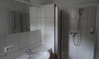 A modern bathroom with white tiles and a clear mirror. There is a shower and a sink with a faucet.