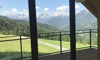 A stunning view of the mountains through a large window. The green meadow and the clear sky create an idyllic atmosphere.