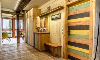 A cozy hallway with wooden paneling and colorful walls. At the end of the hallway, there is a bright room with seating options.