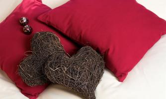 Red cushions are lying on a white background, next to a heart-shaped decorative element made of twigs. In the background, three shiny decorative spheres are visible.