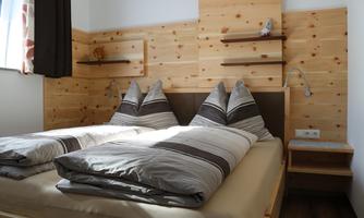 A cozy bedroom with two single beds and wood paneling. The walls are light, and the room is well-lit.